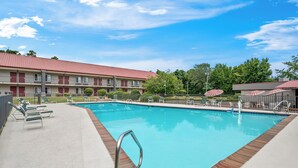 A swimming pool with lounge chairs and a building with a red roof in the background. - Red Roof Inn Hot Springs (Hot Springs)