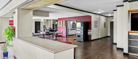 A spacious hotel lobby with a reception desk, a dining area, and a refrigerator vending machine.