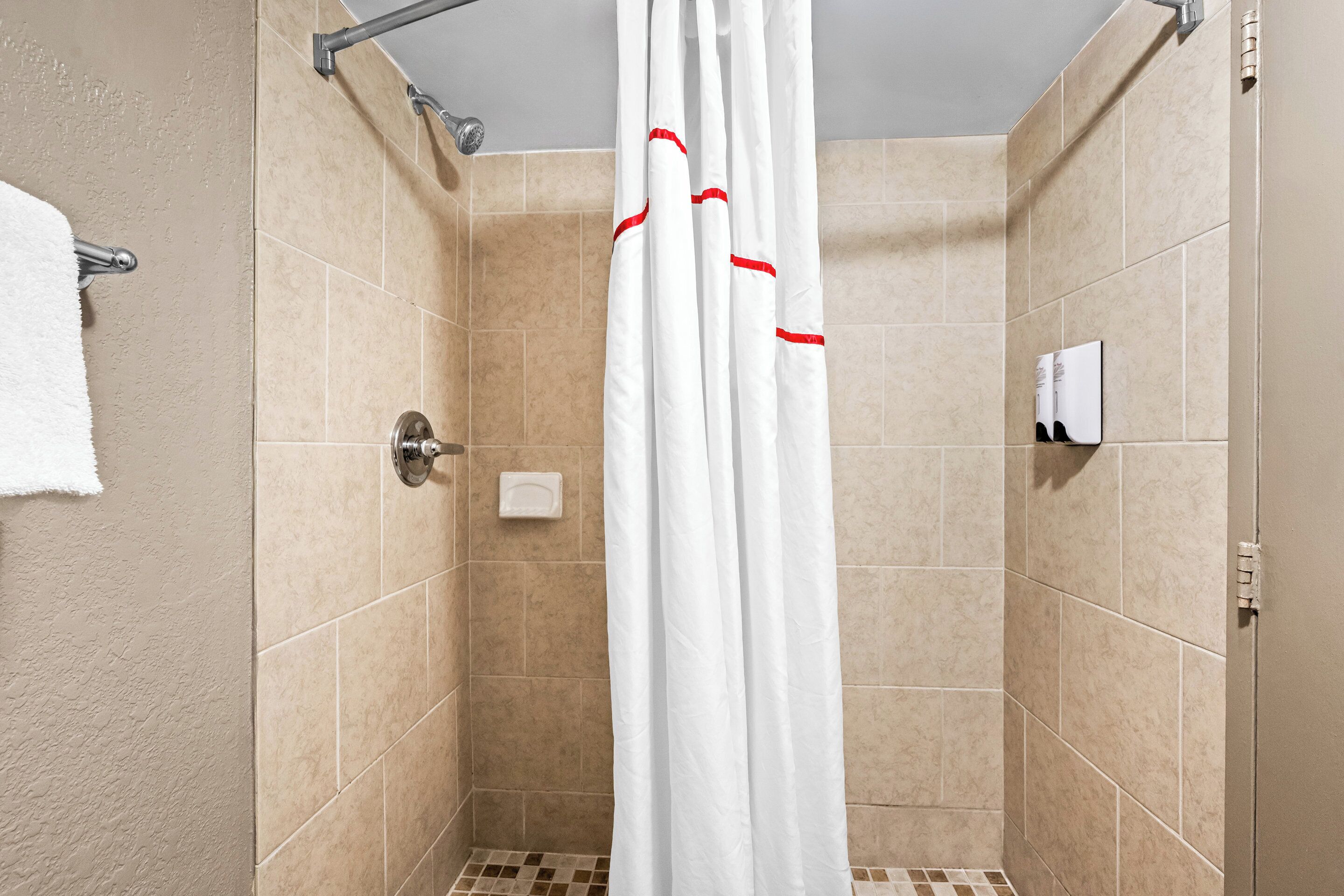 A shower area with beige tiles, a white shower curtain, and a towel rack.