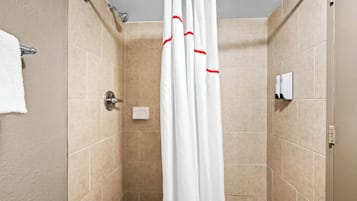 A shower area with beige tiles, a white shower curtain, and a towel rack.