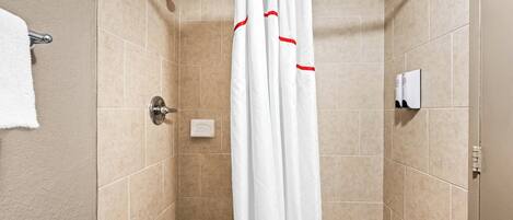 A shower area with beige tiles, a white shower curtain, and a towel rack.