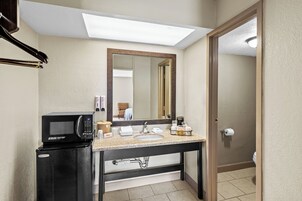 Un bagno d'albergo compatto con lavandino, specchio e forno a microonde su un mobiletto.