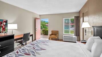 A hotel room with a bed, desk, chair, and a view of the outdoors.