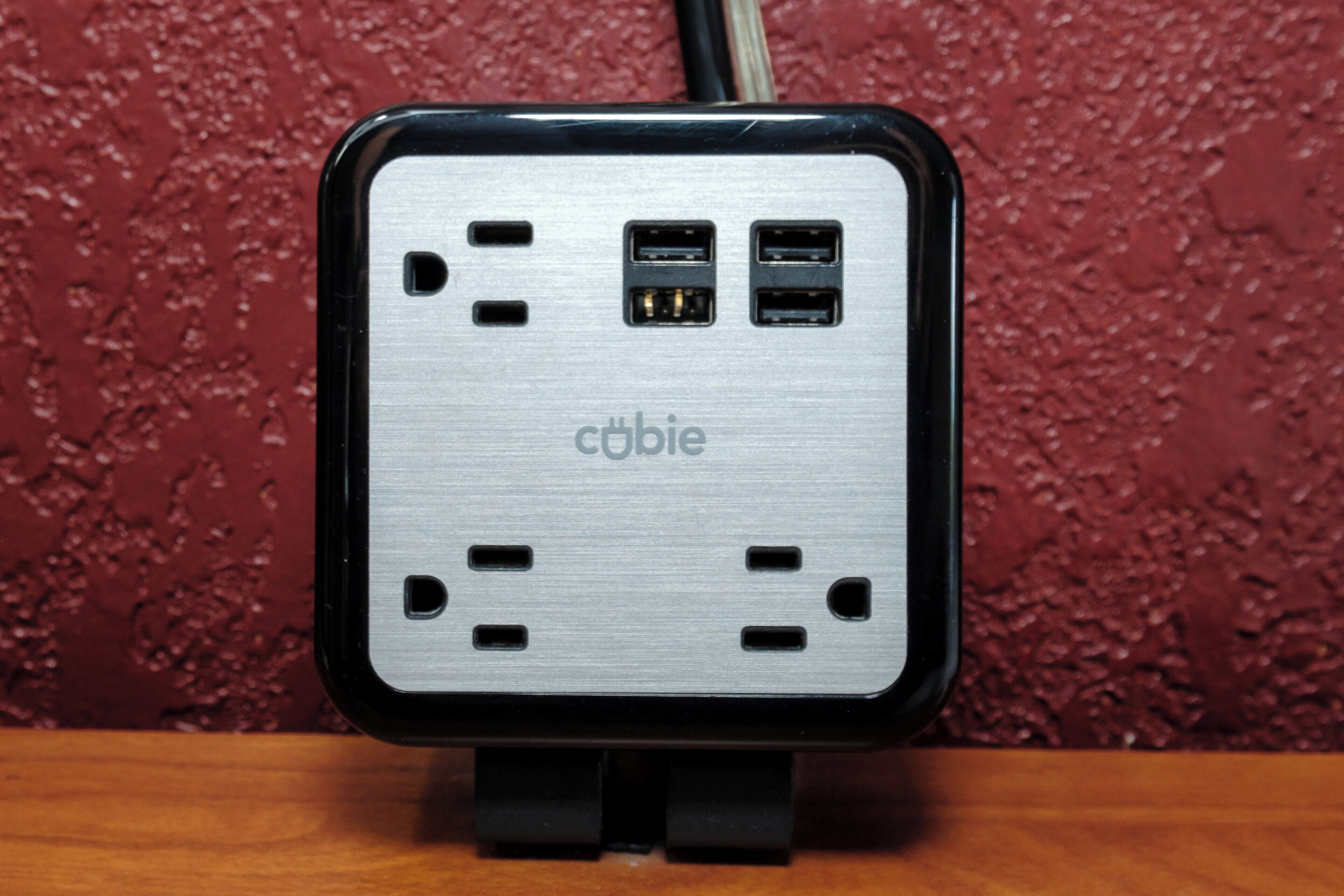 A portable power bank with multiple USB ports and a cable, placed on a wooden surface against a textured wall.