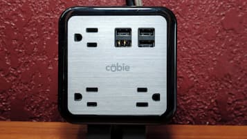 A portable power bank with multiple USB ports and a cable, placed on a wooden surface against a textured wall.