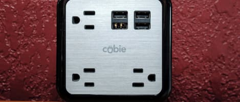 A portable power bank with multiple USB ports and a cable, placed on a wooden surface against a textured wall.