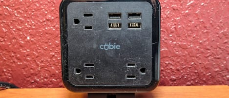 Un dispositivo electrónico negro con varios puertos sobre una superficie de madera frente a un fondo rojo texturizado.