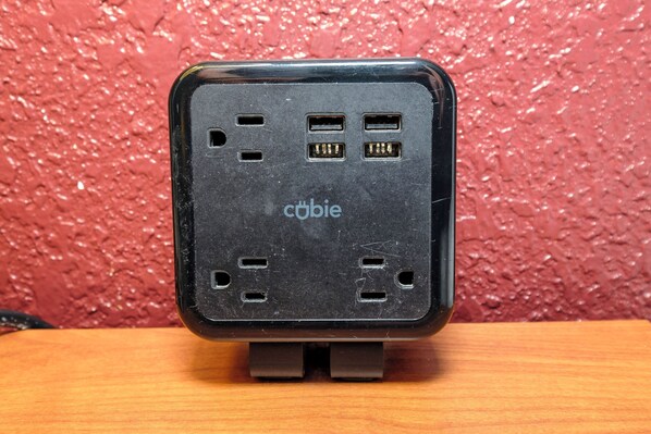 A black electronic device with multiple ports on a wooden surface against a textured red background.