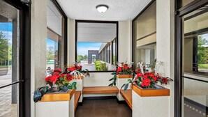 Un couloir agrémenté de bancs et de plantes en pot, qui mène à l’entrée d’un bâtiment.