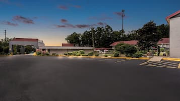 A parking lot with a building that has a red roof and a signboard. There are trees and bushes around the building.