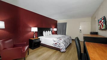 Ein Hotelzimmer mit Bett, Schreibtisch, Stuhl, Nachttisch und Fernseher.