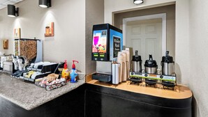 A hotel reception area with a coffee machine, self-service beverage station, and various amenities like hand sanitizer and paper products. - Red Roof Inn Hot Springs (Hot Springs)