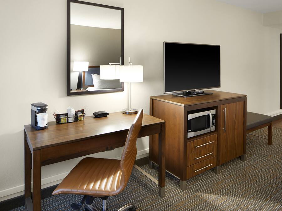 A hotel room with a wooden desk, a television, a microwave, and a chair.