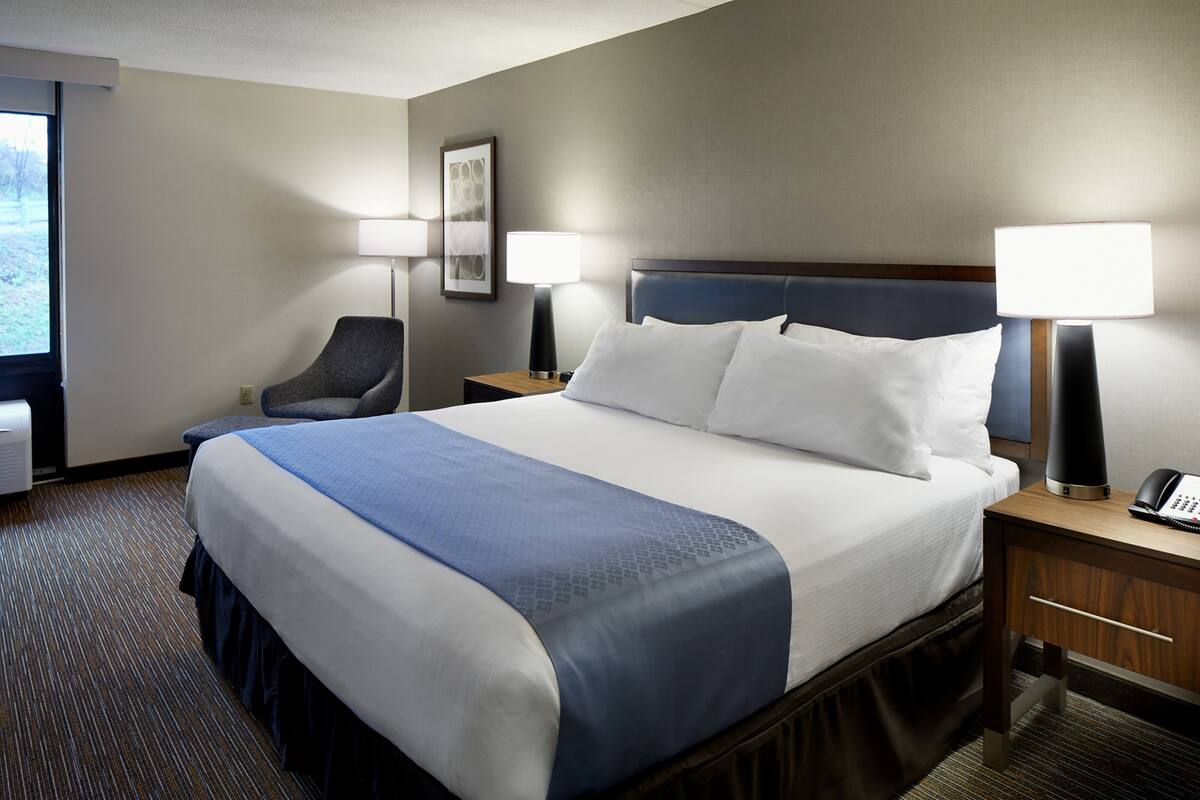 A hotel room with a large bed, two bedside tables, a chair, and two lamps.