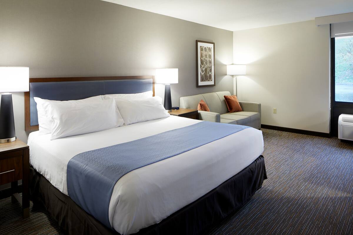 A hotel room with a large bed, a sofa, two lamps, and a framed picture on the wall.