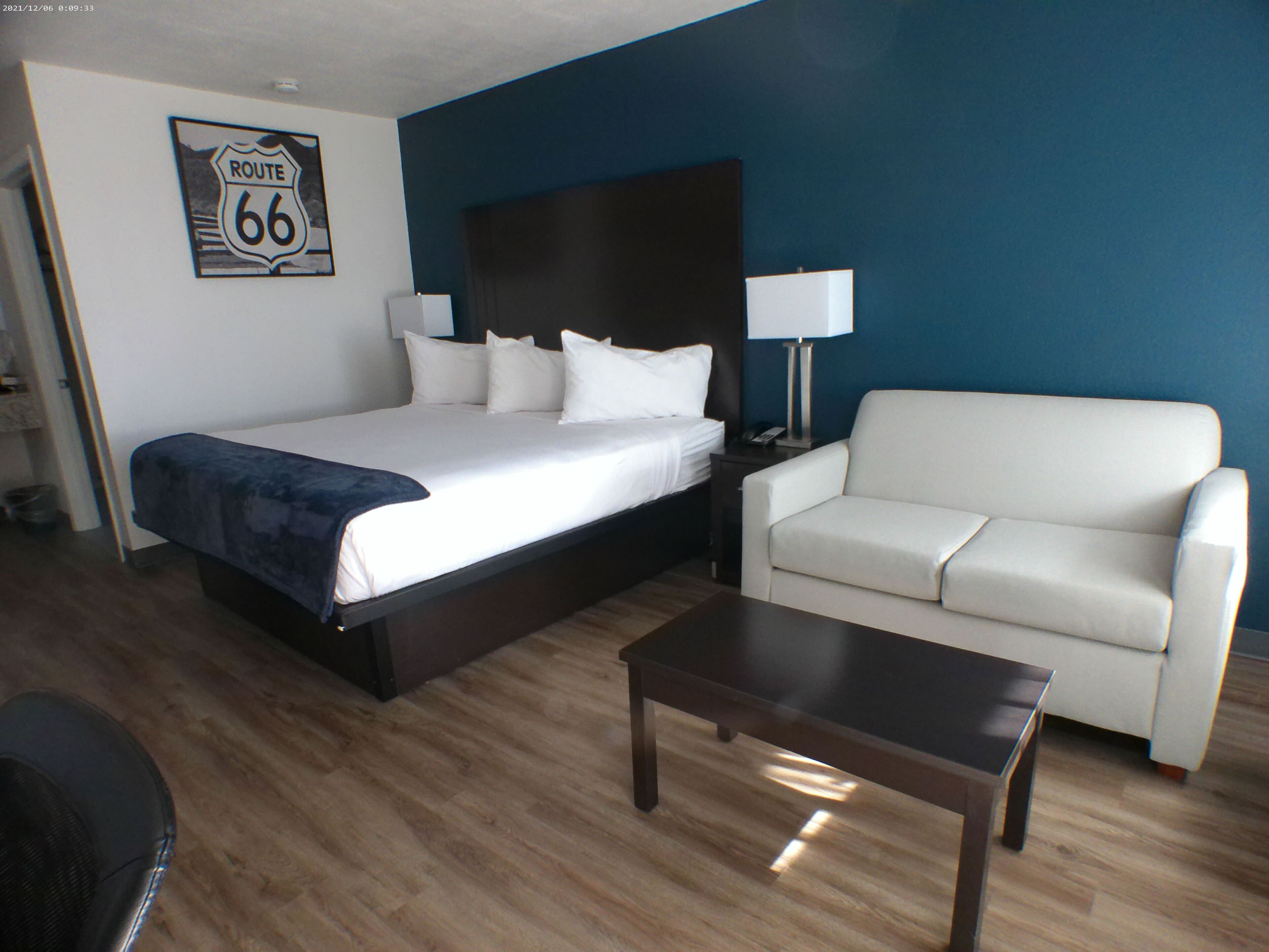 A hotel room with a large bed, a white sofa, a small table, and a lamp.