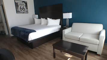 A hotel room with a large bed, a white sofa, a small table, and a lamp.