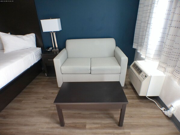 A room with a bed, a white sofa, a small table, a lamp, and a heater.