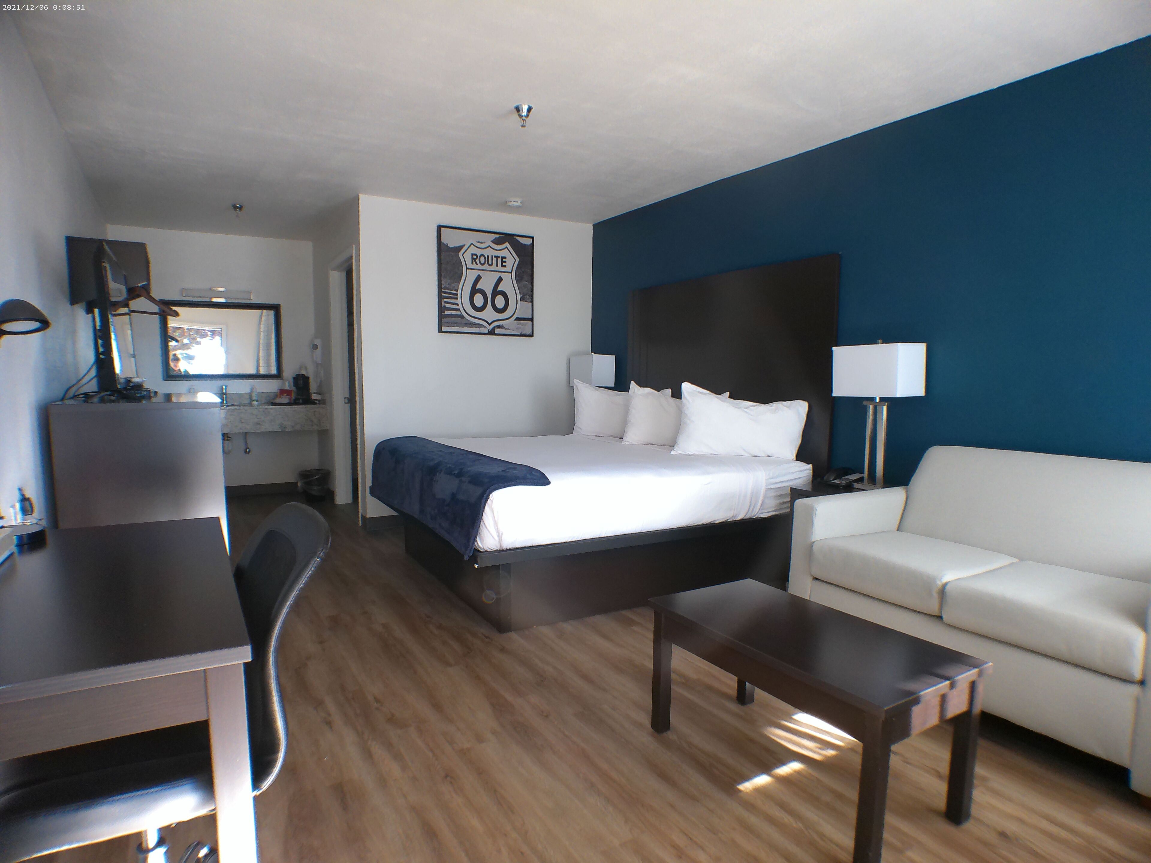 A hotel room with a bed, a desk, a chair, a sofa, and a mirror.