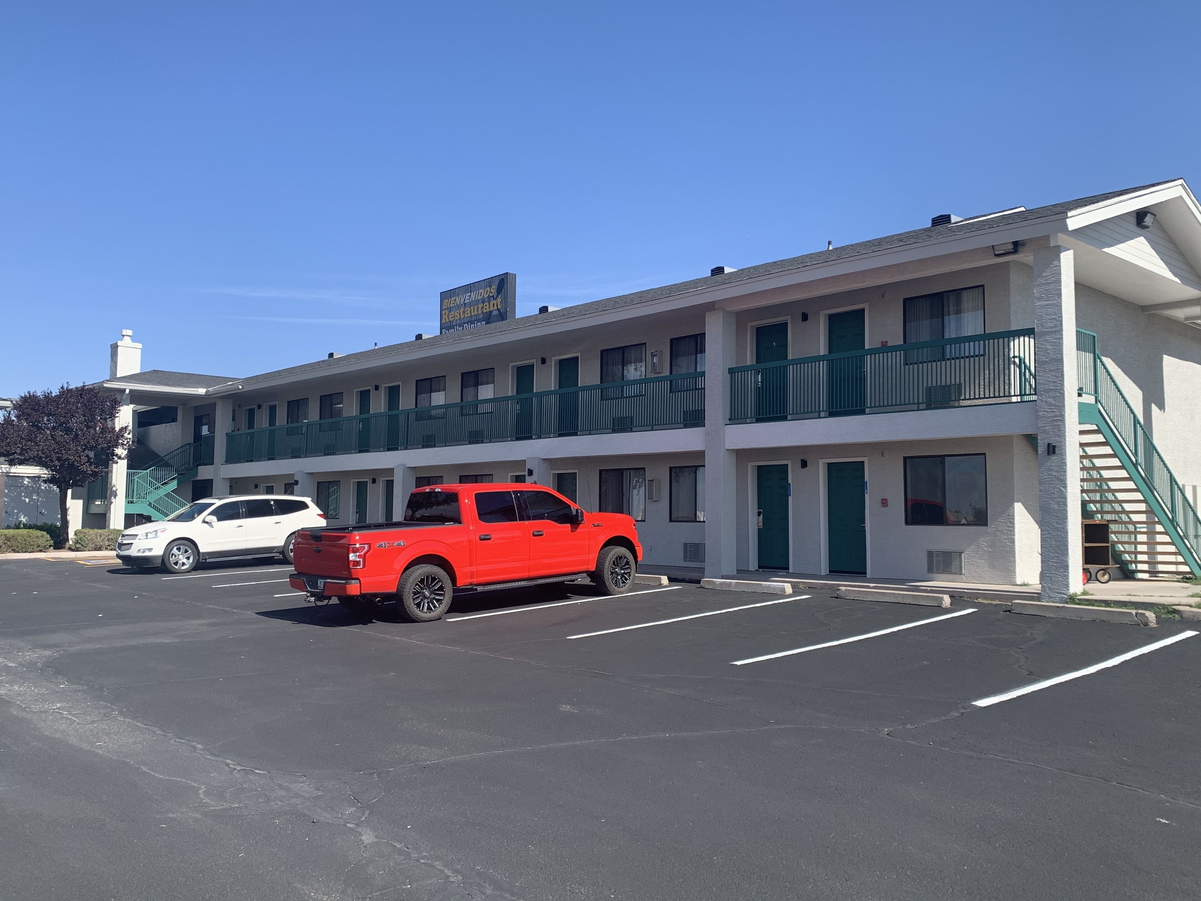 A two-story motel with a green balcony, a parking lot, and a red pickup truck parked in front.