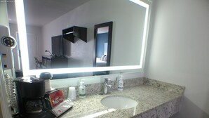 A bathroom with a granite countertop, a sink, a mirror, and a coffee maker. - Greentree Inn Holbrook (Holbrook)