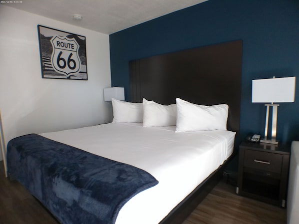 Une chambre d’hôtel avec un grand lit, une tête de lit, une table de chevet avec une lampe et un panneau fixé au mur.