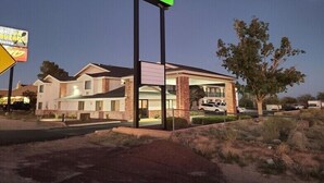 A GreenTree Inn hotel with a prominent green sign, a covered parking area, and a desert landscape. - Greentree Inn Holbrook (Holbrook)