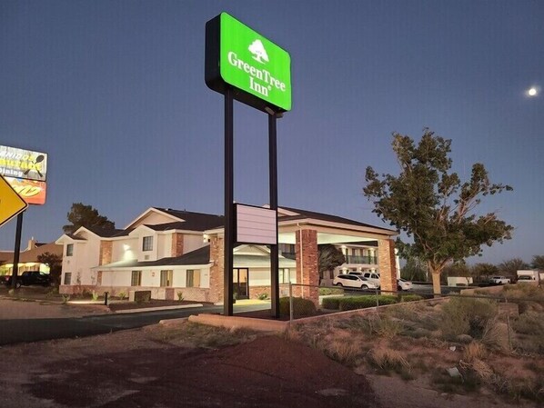 A GreenTree Inn hotel with a prominent green sign, a covered parking area, and a desert landscape.