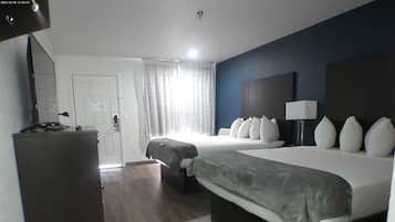 A hotel room with two beds, a desk, a chair, a lamp, and a window with curtains.