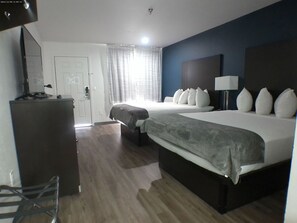 A hotel room with two beds, a desk, a chair, a lamp, and a window with curtains.