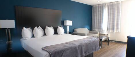 A modern hotel room with a large bed, a sofa, a desk, and a window with curtains.
