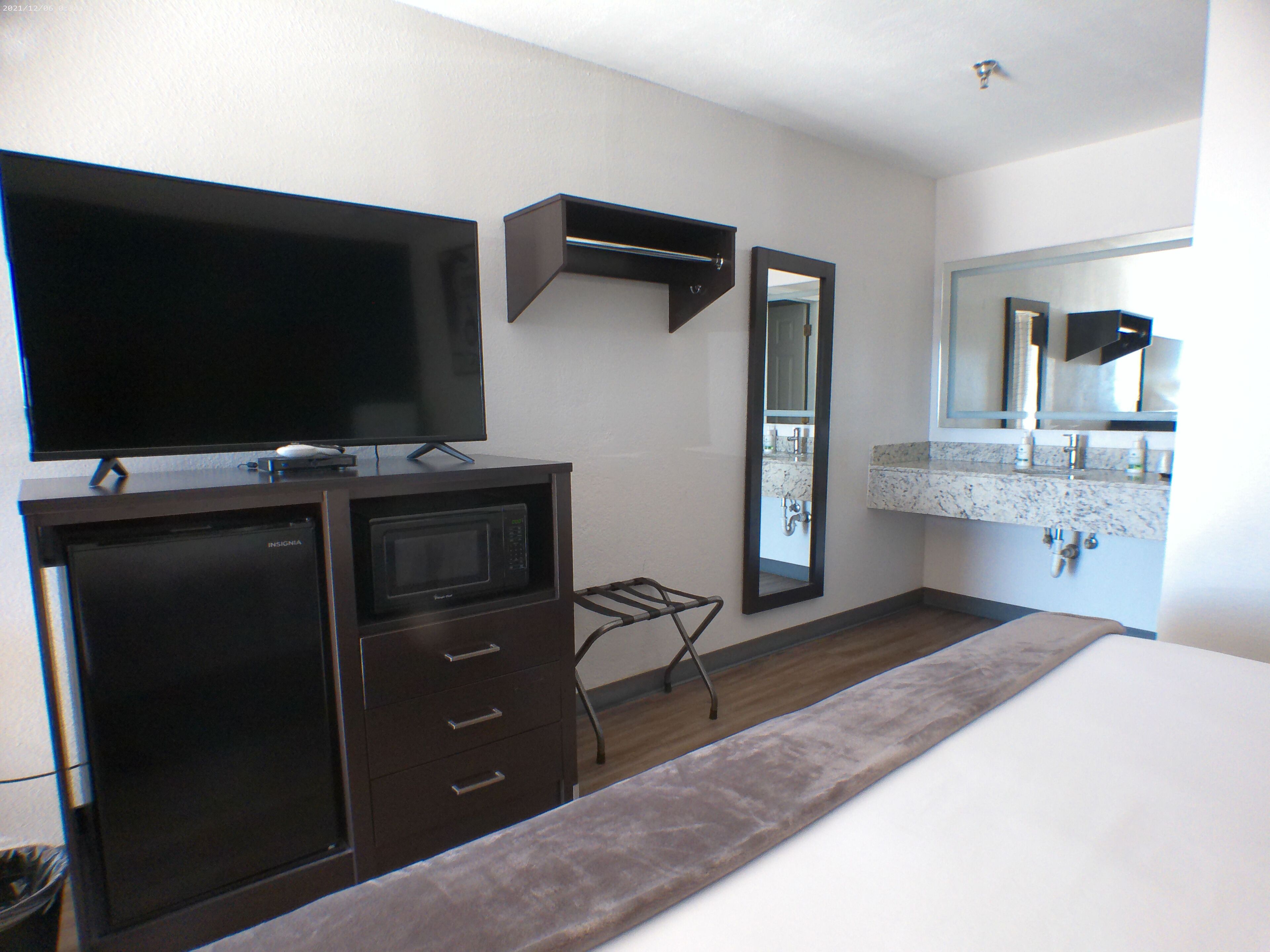 A hotel room with a flat-screen TV, a microwave, a small table, a mirror, and a bathroom with a sink and mirror.