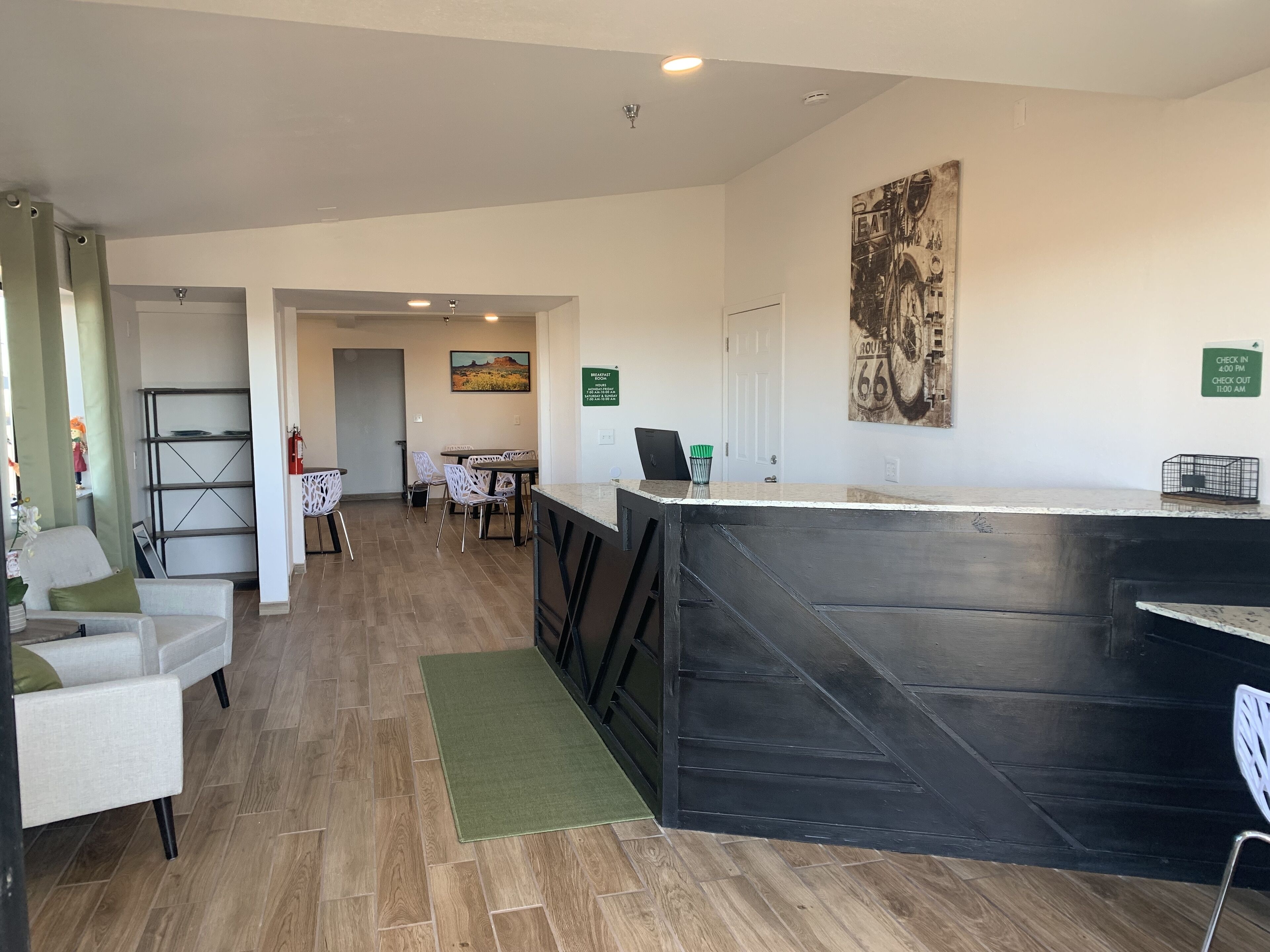 A hotel lobby with a reception desk, a dining area with chairs and a table, and a painting on the wall. - Greentree Inn Holbrook (Holbrook)