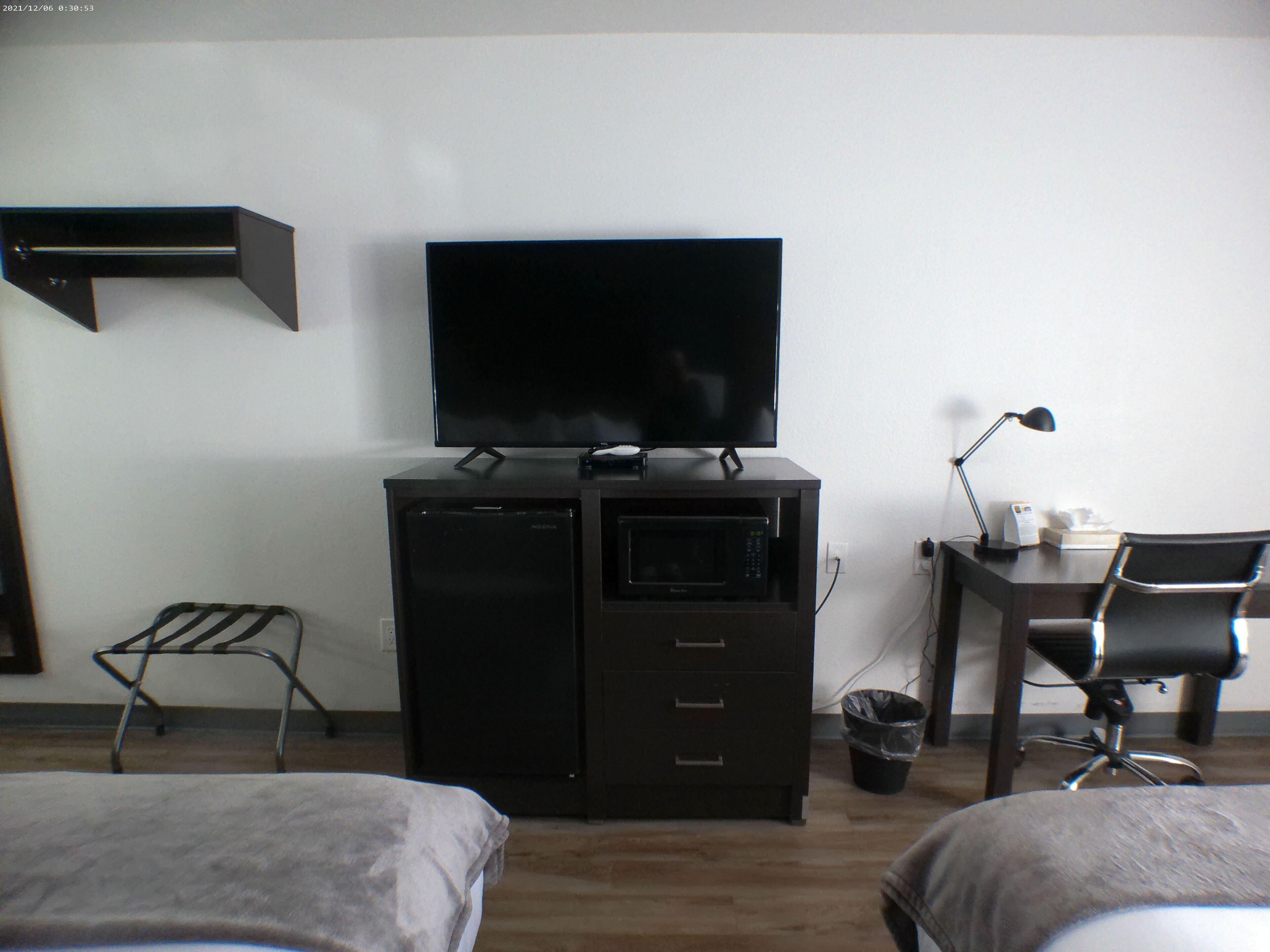 A hotel room with a flat-screen TV on a cabinet, a desk with a lamp, and two beds.