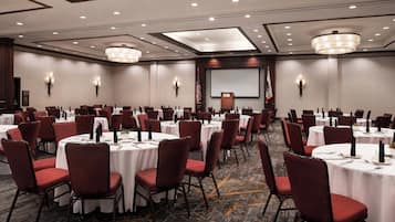 Une salle de conférence avec plusieurs tables rondes, des chaises rouges et un grand écran à l’avant.