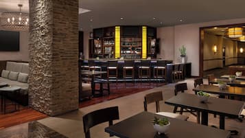 A modern bar area with a stone column, seating, and a bar stocked with bottles.