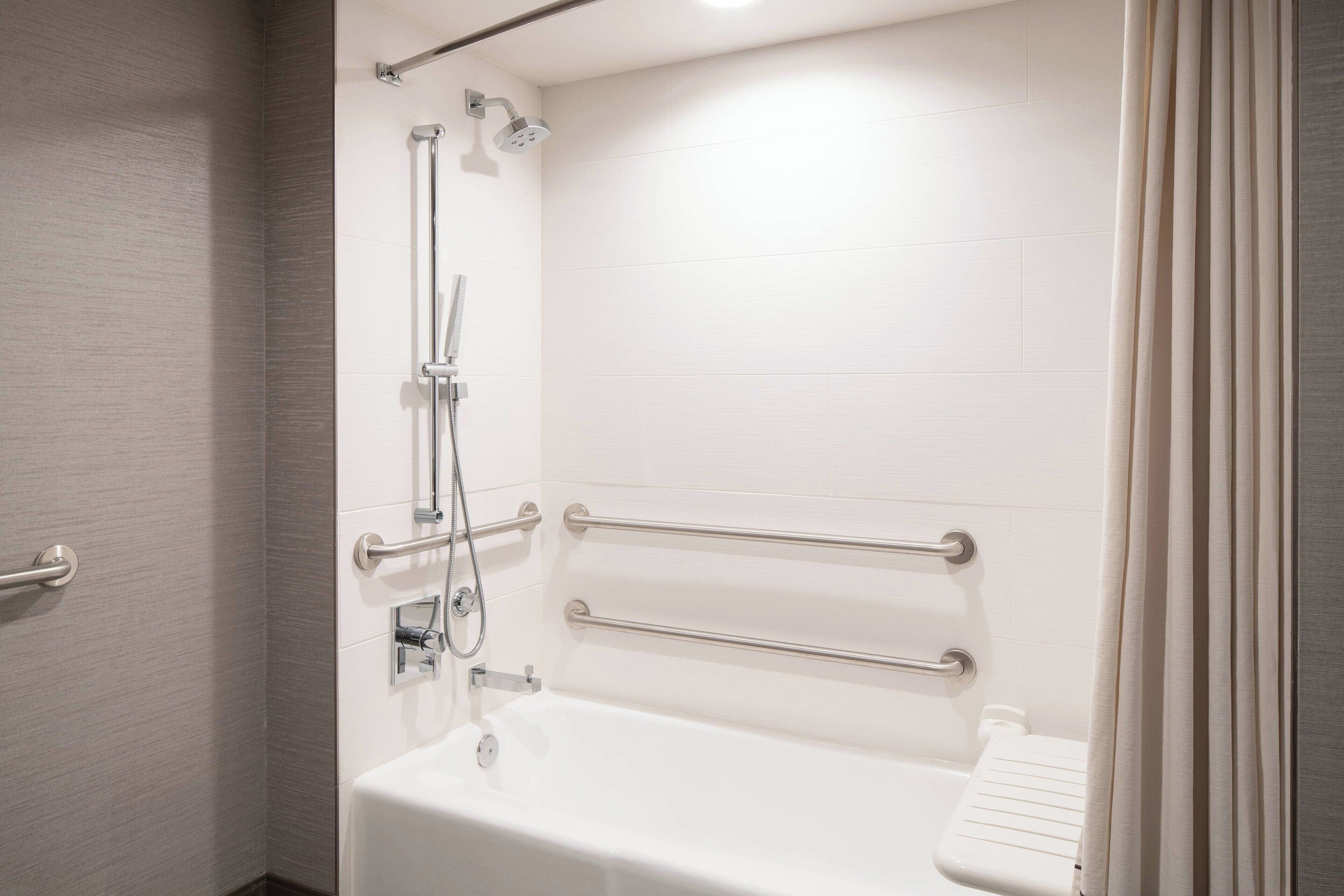 A modern bathroom with a walk-in shower, grab bars, and a white bathtub.