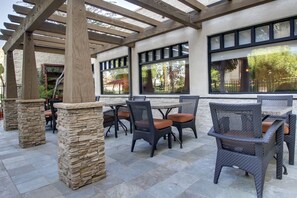 Un patio al aire libre con pilares de piedra, sillas de mimbre y mesas.