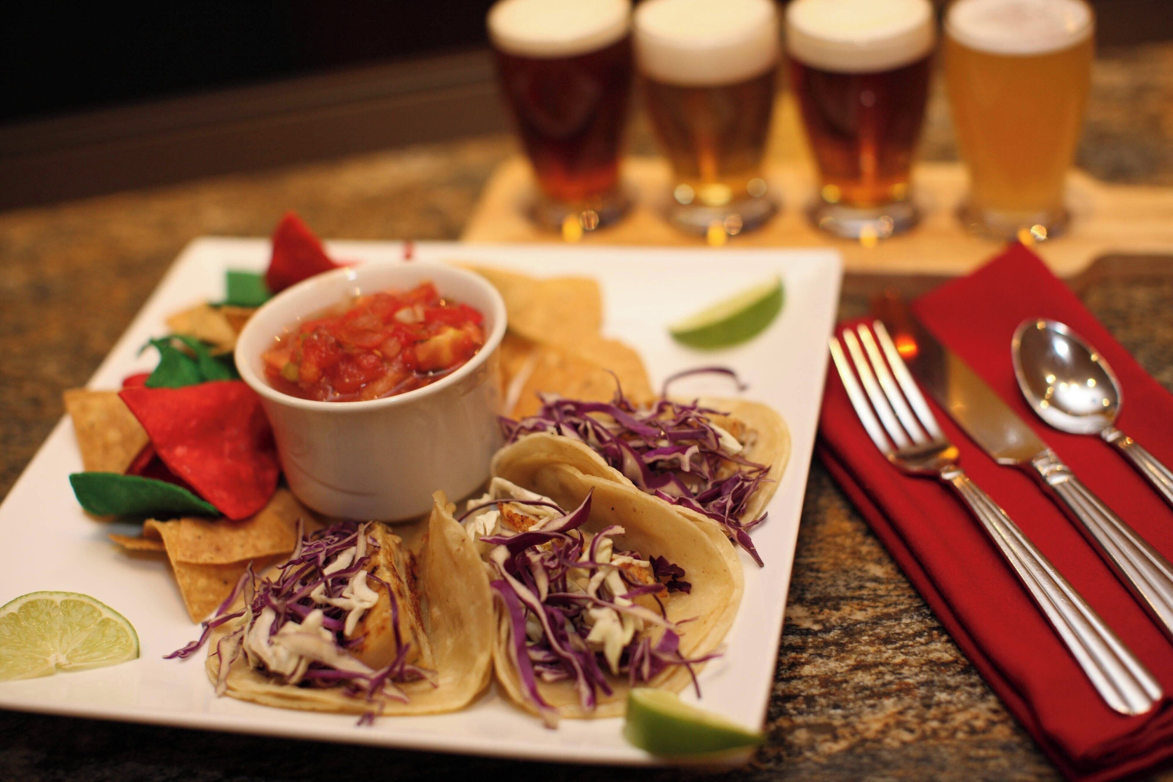 A plate of tacos with a side of salsa and lime, accompanied by a red napkin and cutlery.