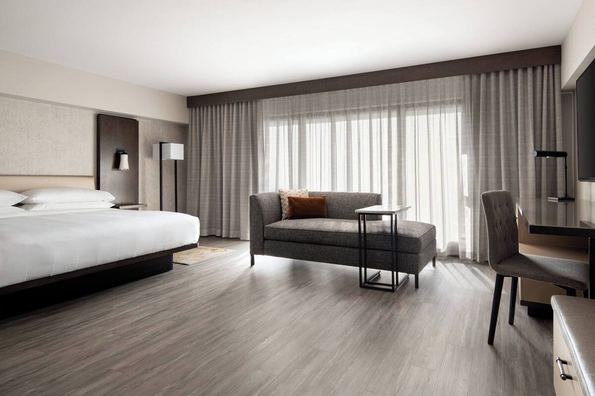 A modern hotel room with a large bed, a sofa, a desk, and a chair.