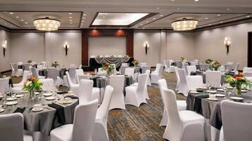 Un salón de banquetes con mesas redondas, sillas blancas y candelabros.