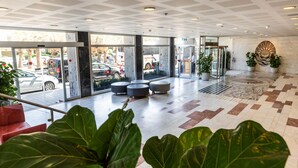 Un vestíbulo moderno con puertas de vidrio grandes, piso estampado y plantas en macetas.