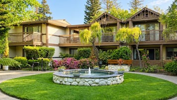 A multi-story building with balconies, a central fountain, and surrounding greenery.