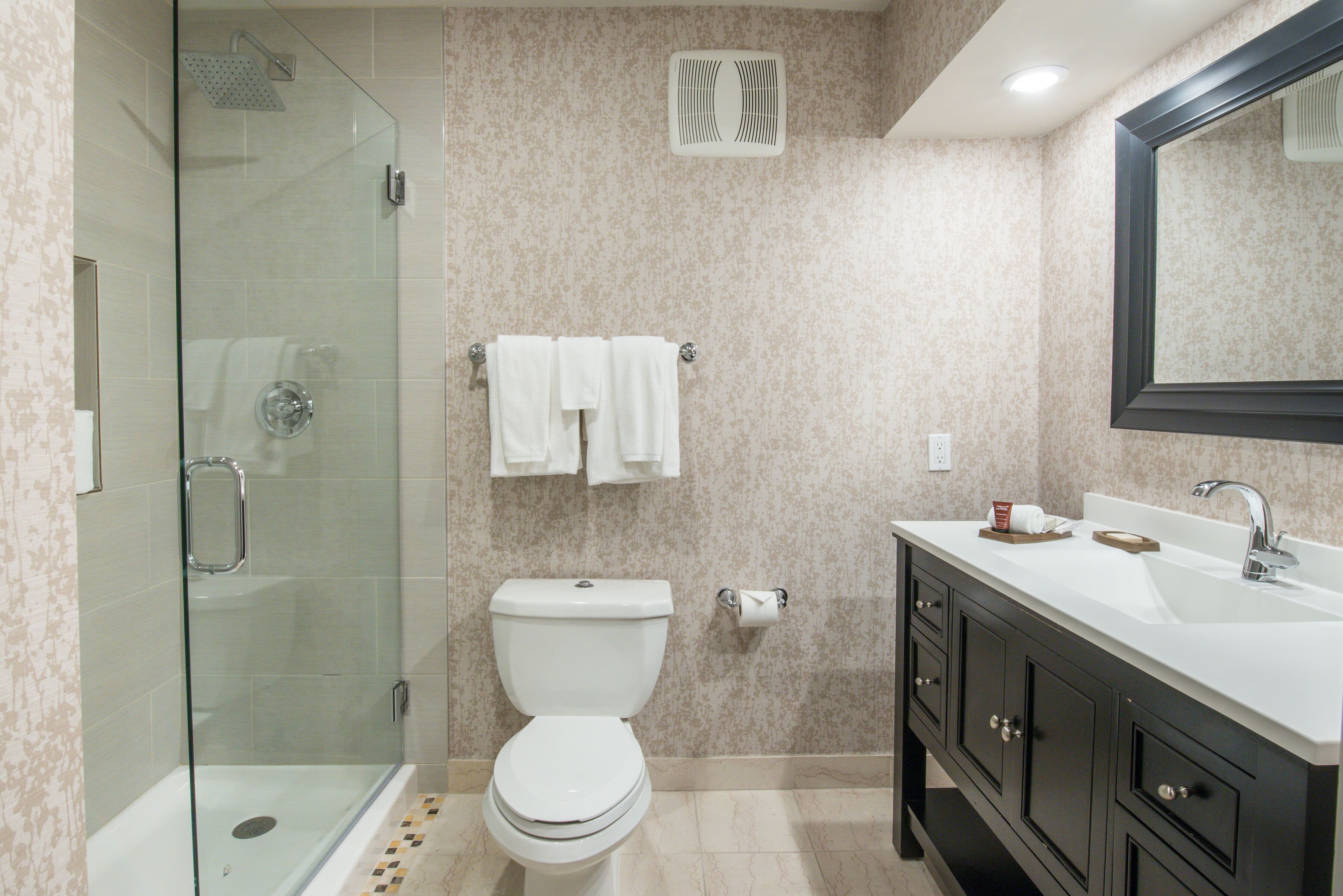 Un baño moderno con ducha de vidrio, inodoro, lavabo y tocador con armarios.