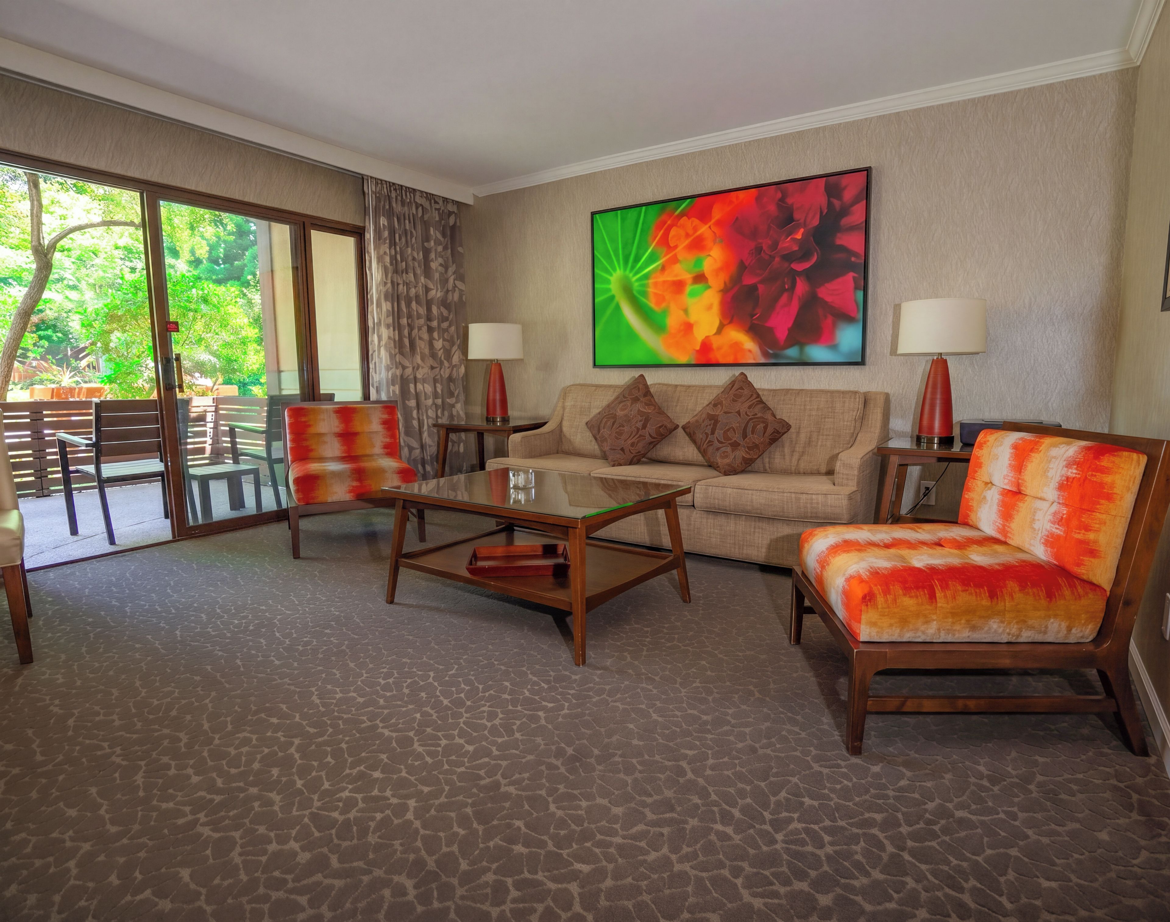 A hotel room with a sofa, armchair, coffee table, and a large window with a view of greenery.