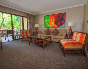 A hotel room with a sofa, armchair, coffee table, and a large window with a view of greenery. - Creekside Inn (Palo Alto)