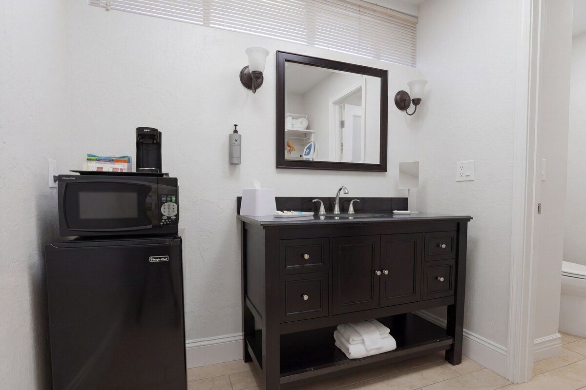 Un bagno compatto con un frigorifero nero, un lavandino con uno specchio sopra e un porta asciugamani sotto.