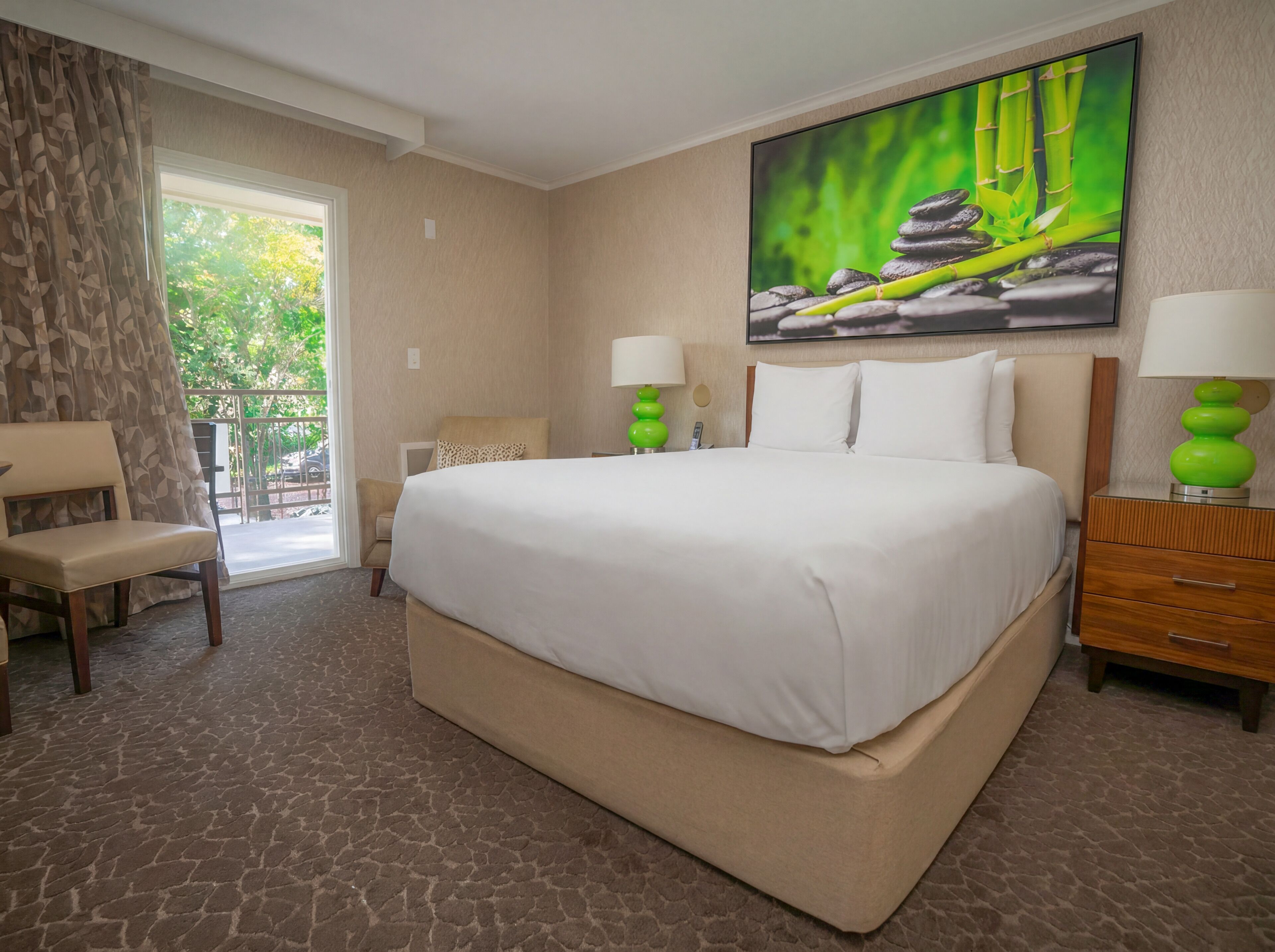 A hotel room with a large bed, a chair, a desk, and a window with a view of greenery.