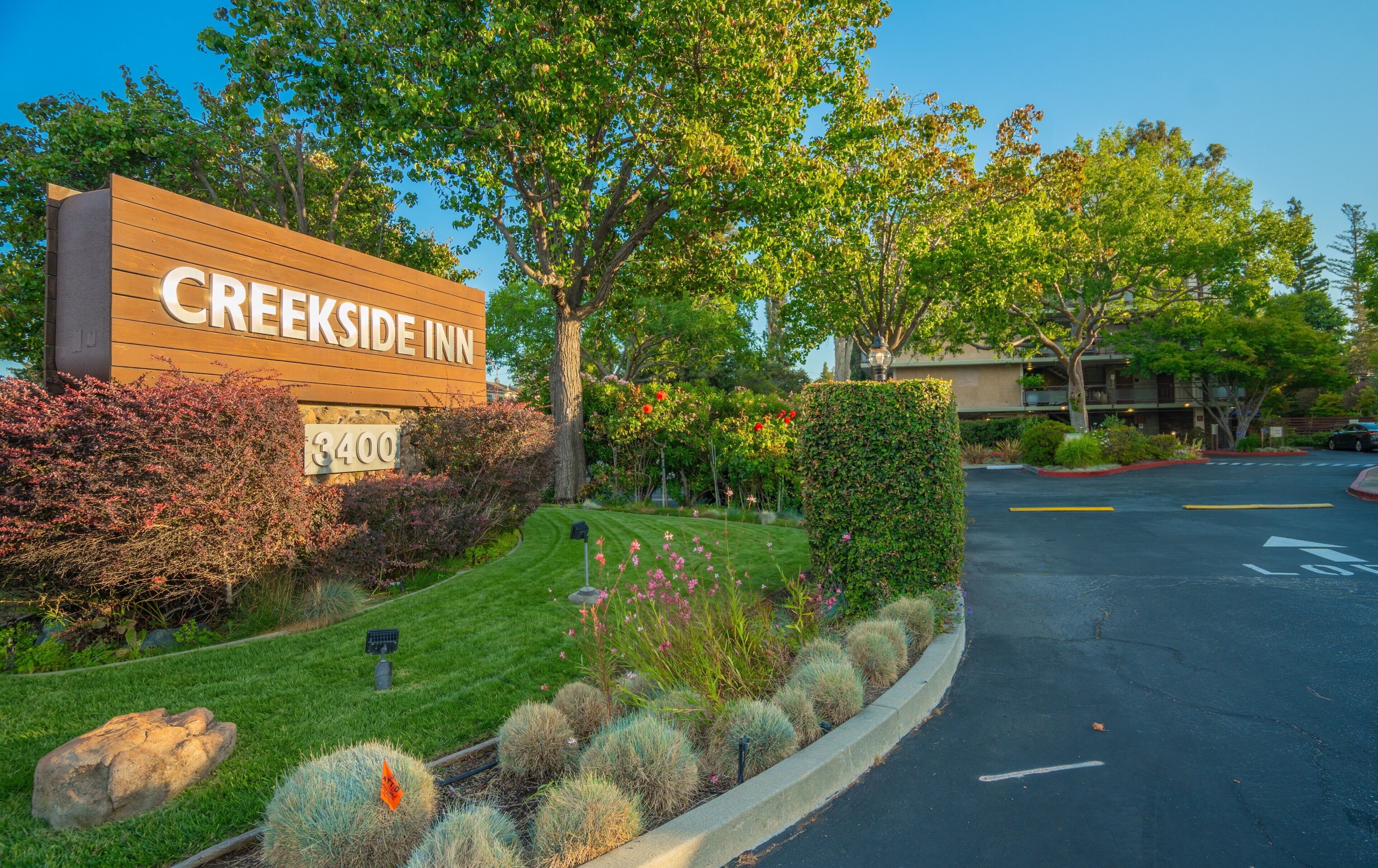 A sign for Creekside Inn with a number 3400, surrounded by landscaped greenery and a parking area.