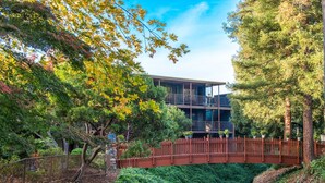 A modern building with a glass facade, surrounded by lush greenery and a wooden bridge. - Creekside Inn (Palo Alto)